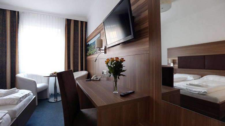 Modern eingerichtetes Hotelzimmer mit Doppelbett, Schreibtisch, Flachbildfernseher und Blumenstrauß.
