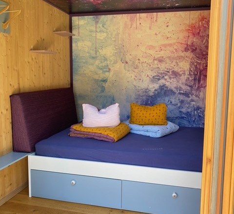 Kleines, gem&uuml;tliches Zimmer mit einem Bett und bunten Kissen.