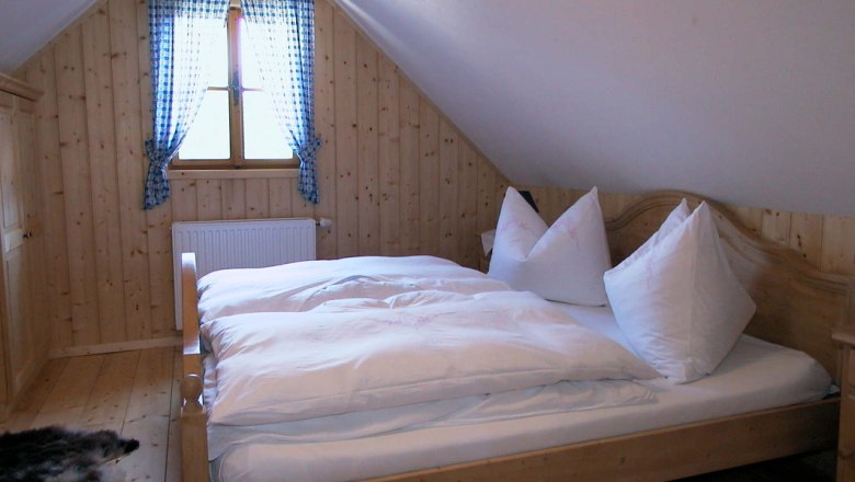 Gemütliches Schlafzimmer mit Holzwänden, einem Doppelbett und einem Fenster mit blau karierten Vorhängen.